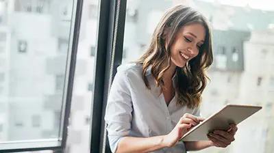 Applied Analytics A woman standing beside an open window while using a tablet