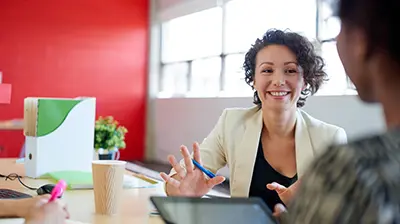 Woman dressed in business casual attire sitting with colleagues smiling.