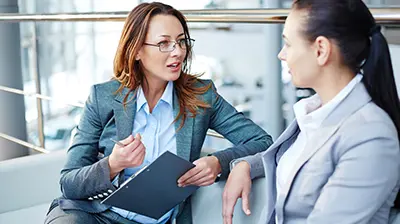 Wealth Track Woman dressed in business attire sitting on a couch and conversing.