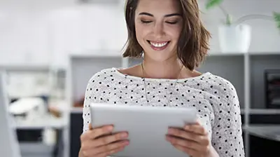 You Can Get There From Here: 7 Steps to Help You Map Out a Successful Digital Journey A woman in a black and white polka dot blouse smiling down at a tablet that she is holding with both hands