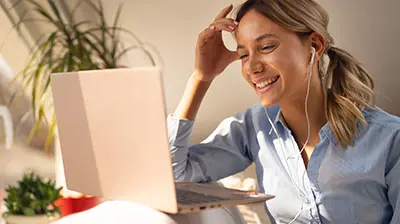 Introducing the New Applied Product Release Hub A woman wearing earphones while laughing at something on her laptop. Her right hand is touching her forehead.