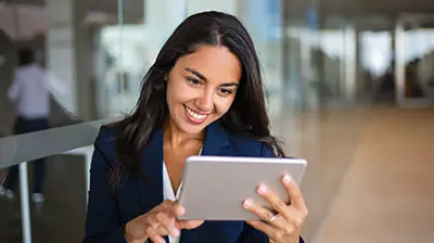Shaping the Future of Insurance Technology A woman in business attire smiling at a tablet while holding it with both hands
