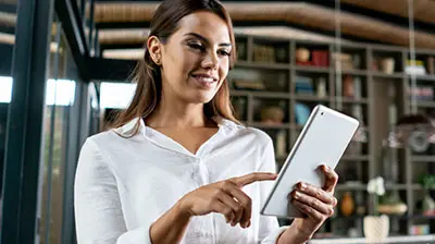 Your Winning Ticket to the Digital Roundtrip of Insurance A woman in a white blouse smiling and pointing at a tablet in her hand.