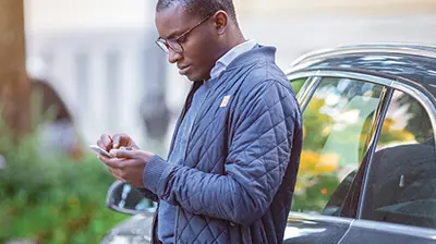 Applied Webrater Man dressed in casual attire leaning on car door using a phone.