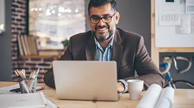 The Digital Path Forward: Are You Ready?  A man sitting at a desk, smiling while using his laptop