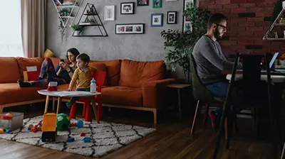 The Future Is Now: A Guide to Adapting Your Brokerage to the New Norm A family in their living room with the father working at his desk while the kids are lounging on the couch.