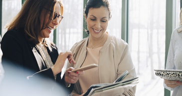 Alliance Partners Two women in casual attire both looking down at a phone in one woman's hand.