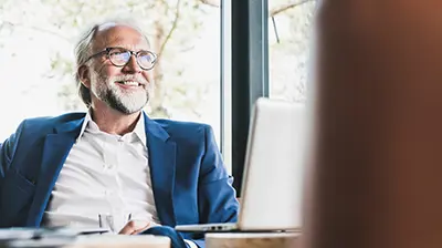 The 5 Benefits of Being a Digital Agency: Growth A man wearing a blue blazer smiling while sitting at a desk in front of a laptop