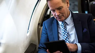 Insight Customer Self Service Man in business attire sitting on an airplane using a tablet.