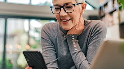 A woman resting a hand on her neck while smiling at her smart phone
