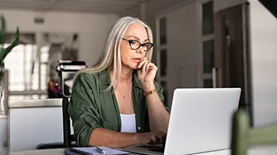 The Digital Path Forward: Harnessing Commercial Lines A woman sitting at her kitchen table, using her laptop while resting a hand on her chin